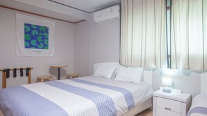 A hotel room with a bed, bedside tables, a small table, a wall-mounted air conditioner, and a window with curtains. - Jeong House (Seoul)