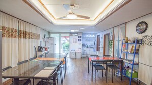 A dining area with a glass table, chairs, a ceiling fan, and a kitchen in the background. - Jeong House (Seoul)