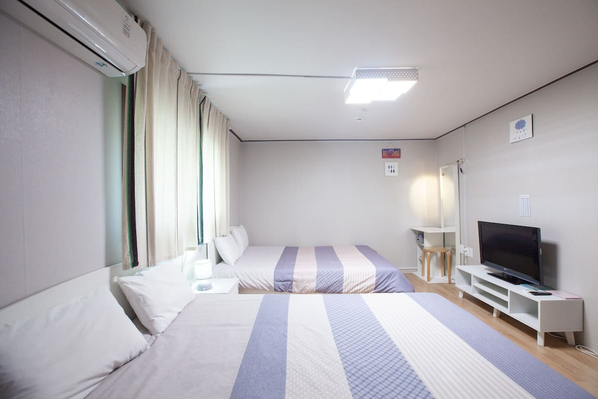 A hotel room with two beds, a TV, a desk, and a window with curtains.