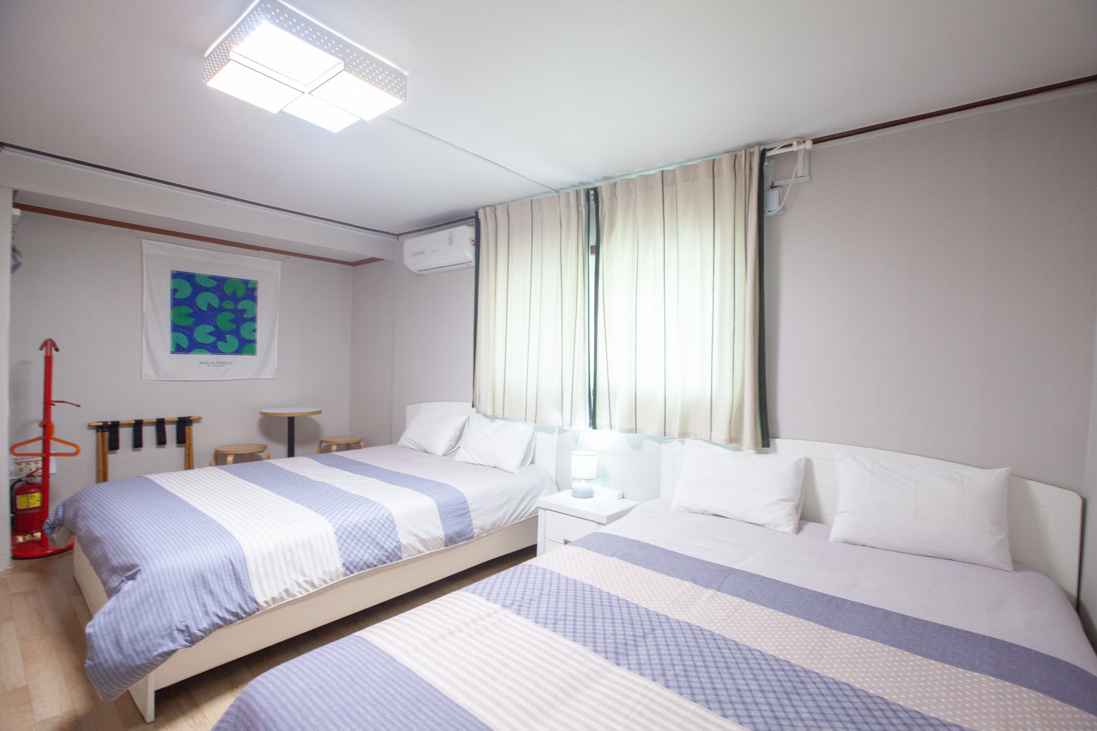 Hotellihuone, jossa on kaksi sänkyä, pieni pöytä, tuoli, sammutin ja ikkuna, jossa on verhot.