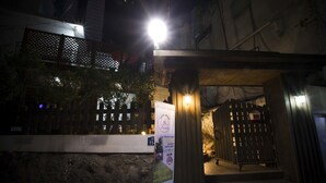 A building entrance at night with a lit signboard, a wooden gate, and a stone wall. - Jeong House (Seoul)