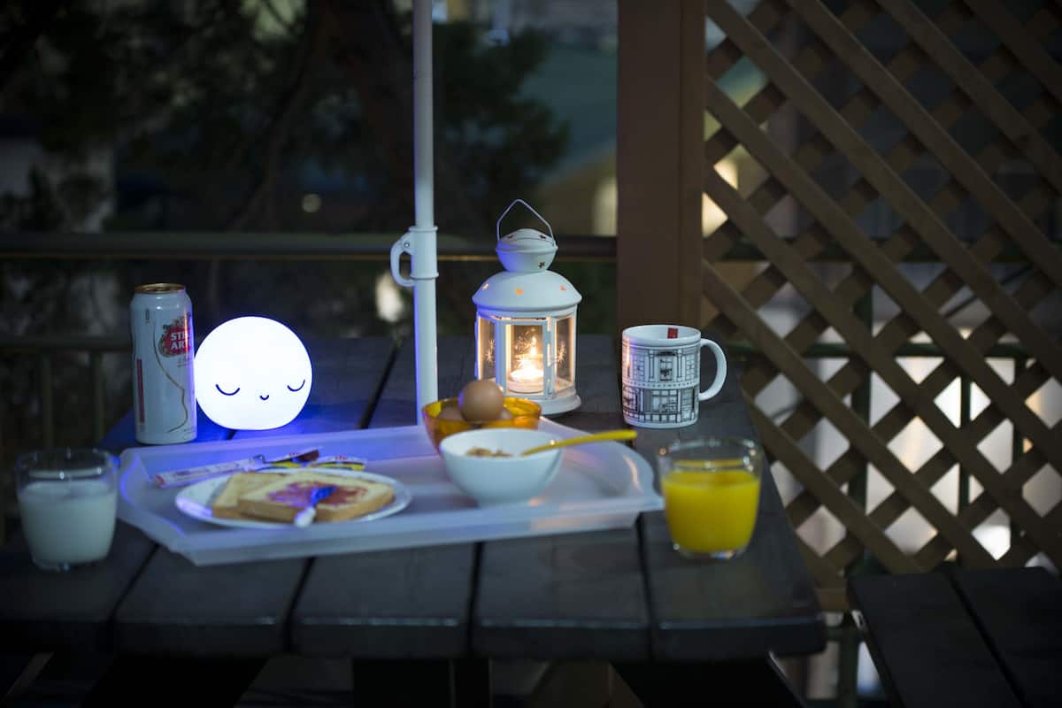 A table set with breakfast items, including toast, eggs, and orange juice, on a wooden deck with a lantern and a can of soda.