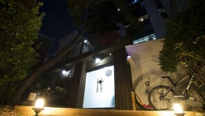 A building entrance with a bicycle leaning against the wall, a door with a clock, and two lit candles on the steps. - Jeong House (Seoul)