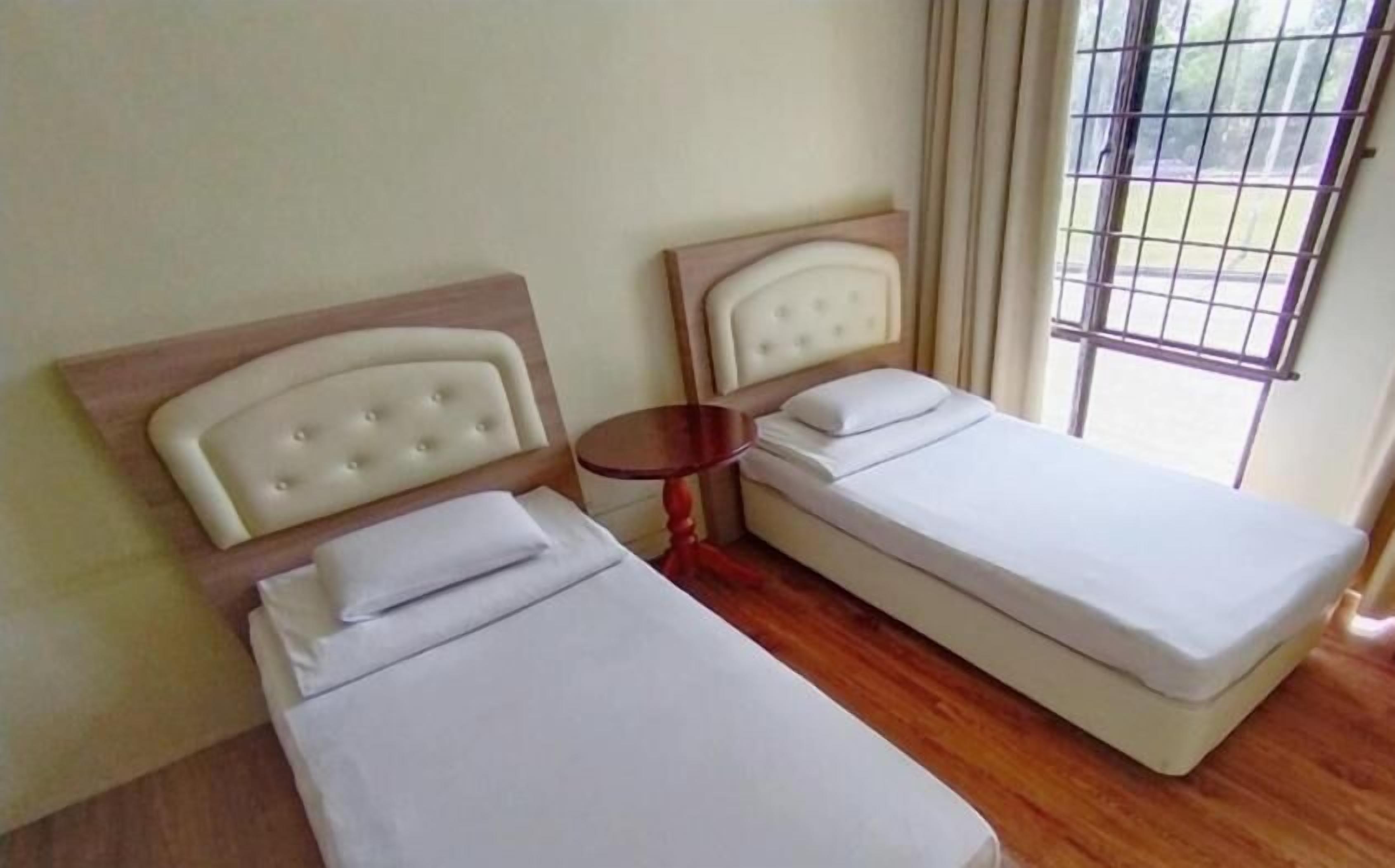A room with two beds, a small round table, and a window with a view of greenery.