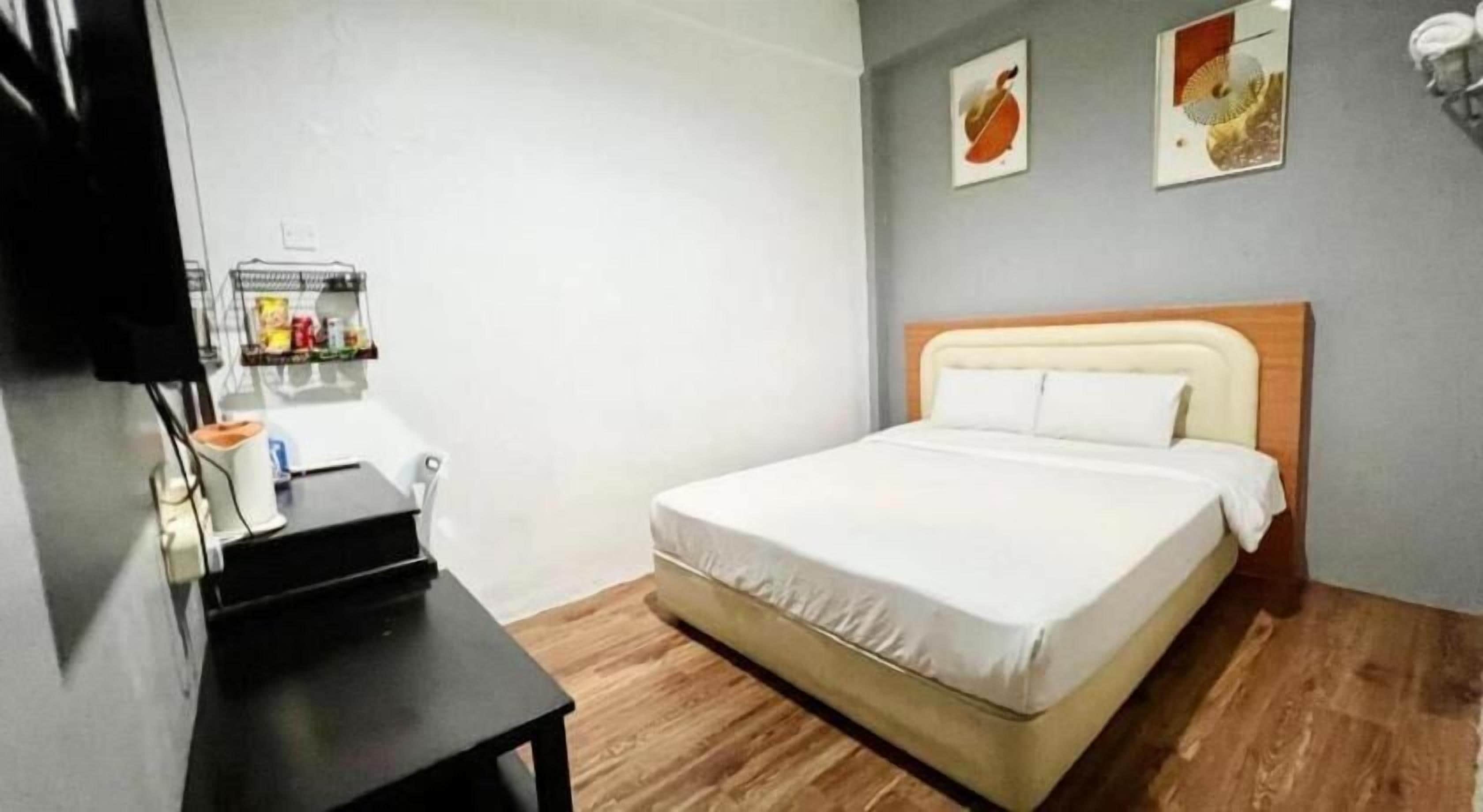 A hotel room with a bed, a desk, and a shelf with items.