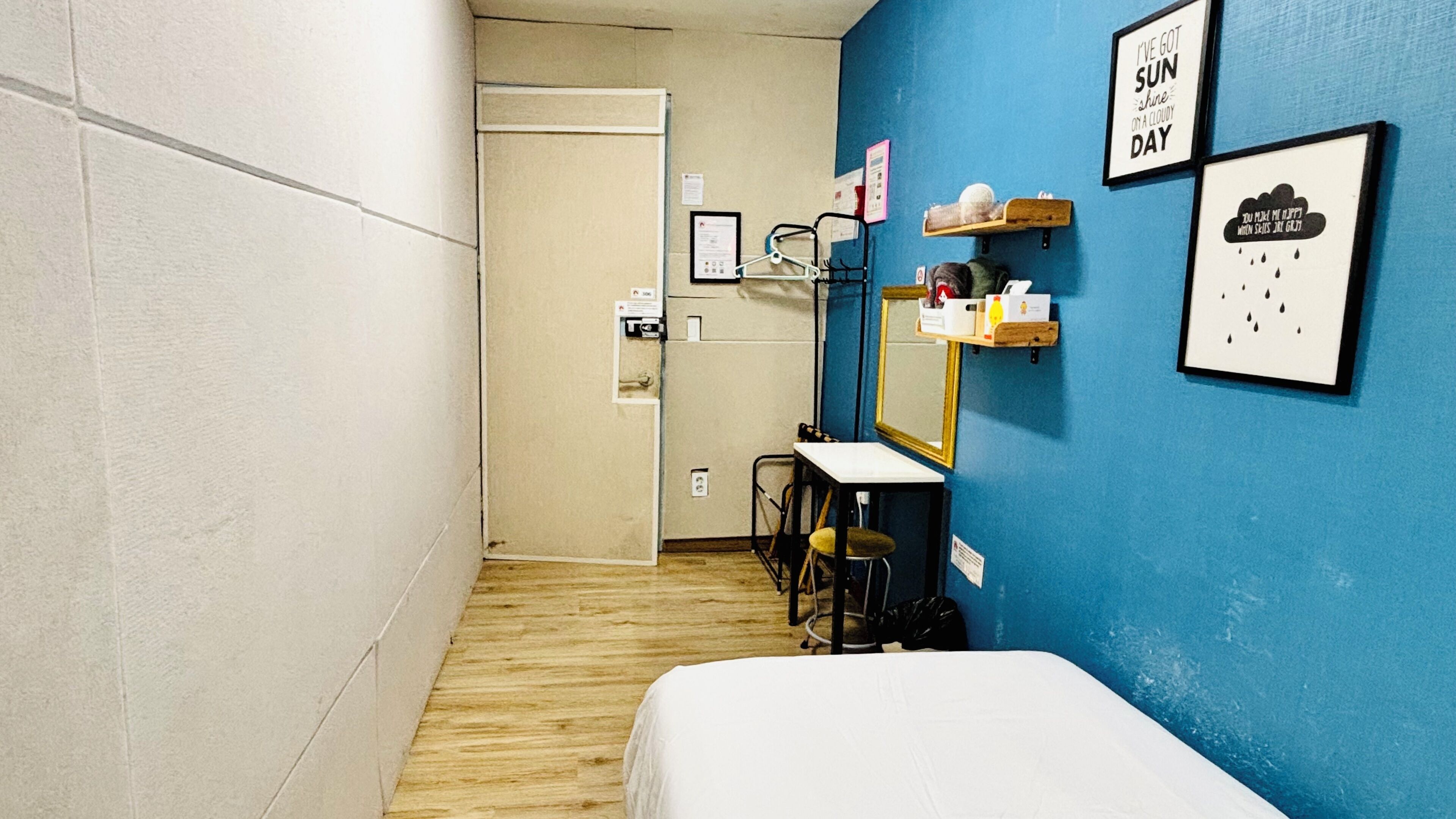 A hotel room with a bed, a desk, a chair, a mirror, and a blue wall with framed quotes.