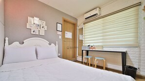 Quarto com uma cama, uma escrivaninha, dois banquinhos, uma porta e uma janela com persianas.