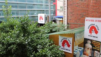 A guesthouse with a signboard, a brick wall, and a glass building in the background.