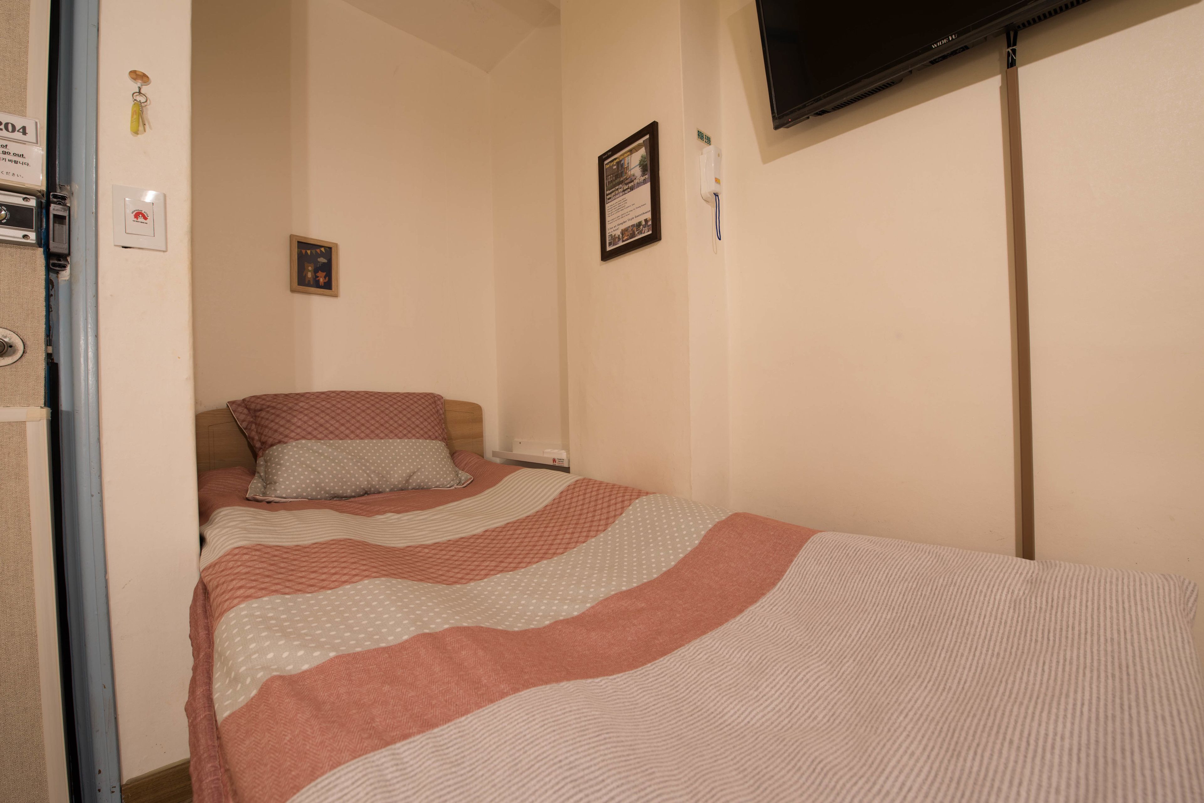 Quarto com cama, televisão na parede e porta com puxador.