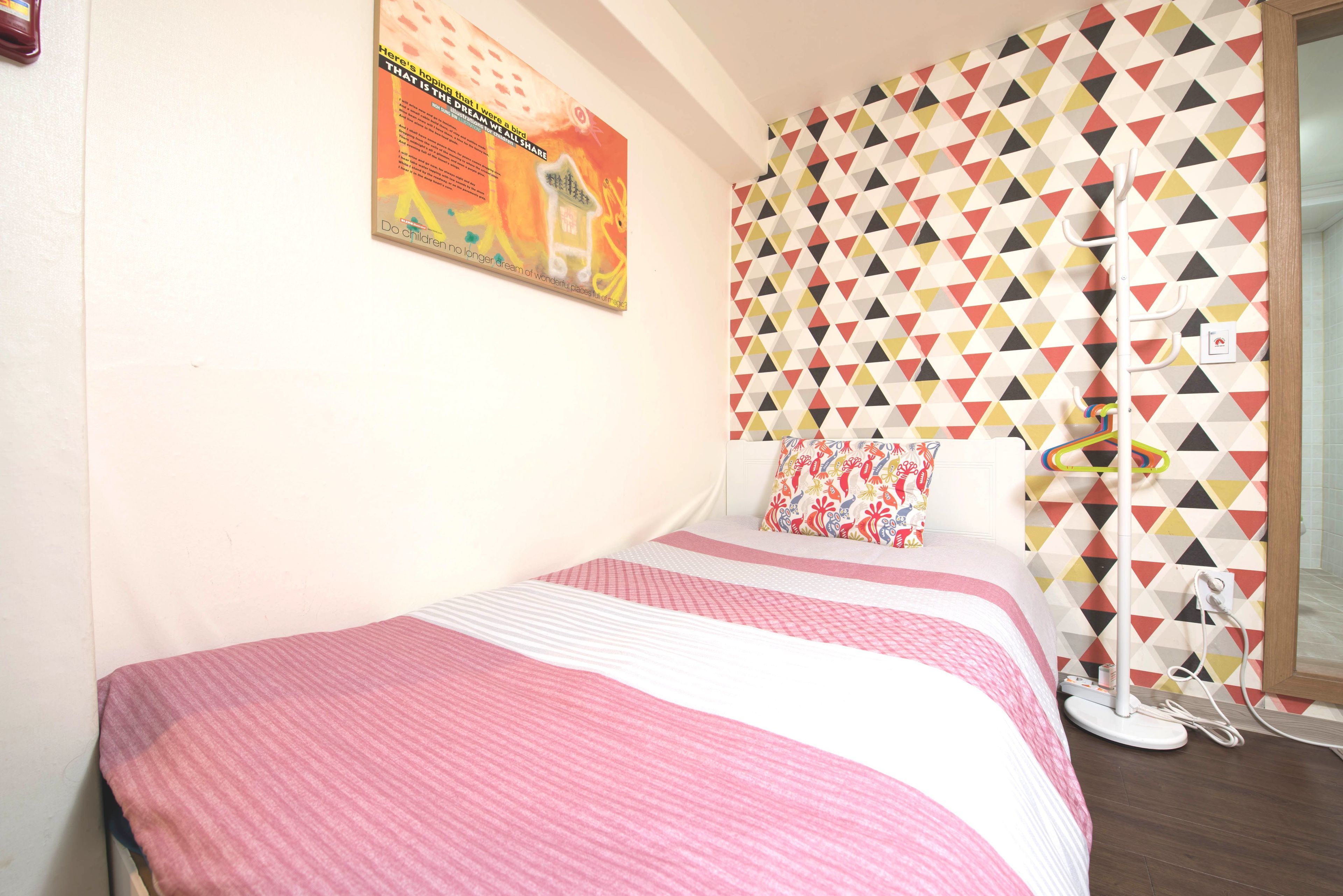 Un dormitorio con una cama, una pared con un estampado geométrico colorido y un cartel en la pared.