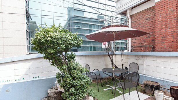 Um terraço no telhado com uma pequena árvore, uma mesa com cadeiras e um guarda-sol grande.