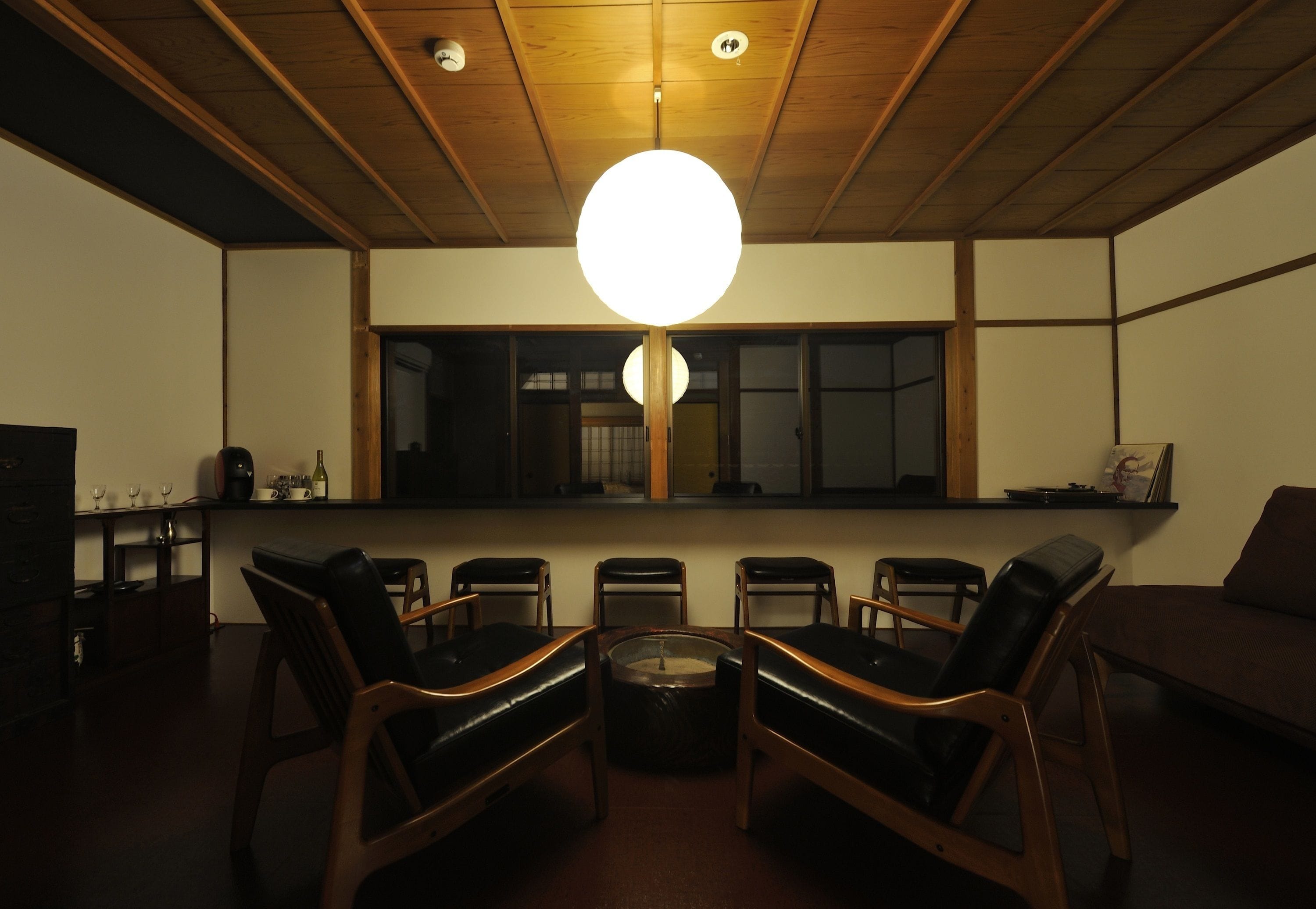 A dimly lit room with a round table and six chairs, a wooden ceiling, and a large window.