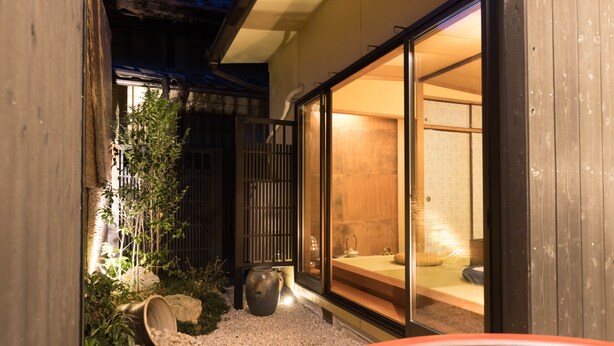 A traditional Japanese building with a wooden exterior, a gravel pathway, and a large sliding glass door leading to an interior space with a tatami mat room. - Kiraku Kyoto Higashiyama (Kyoto)