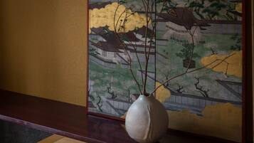 A vase with branches on a wooden table in front of a traditional Japanese painting.