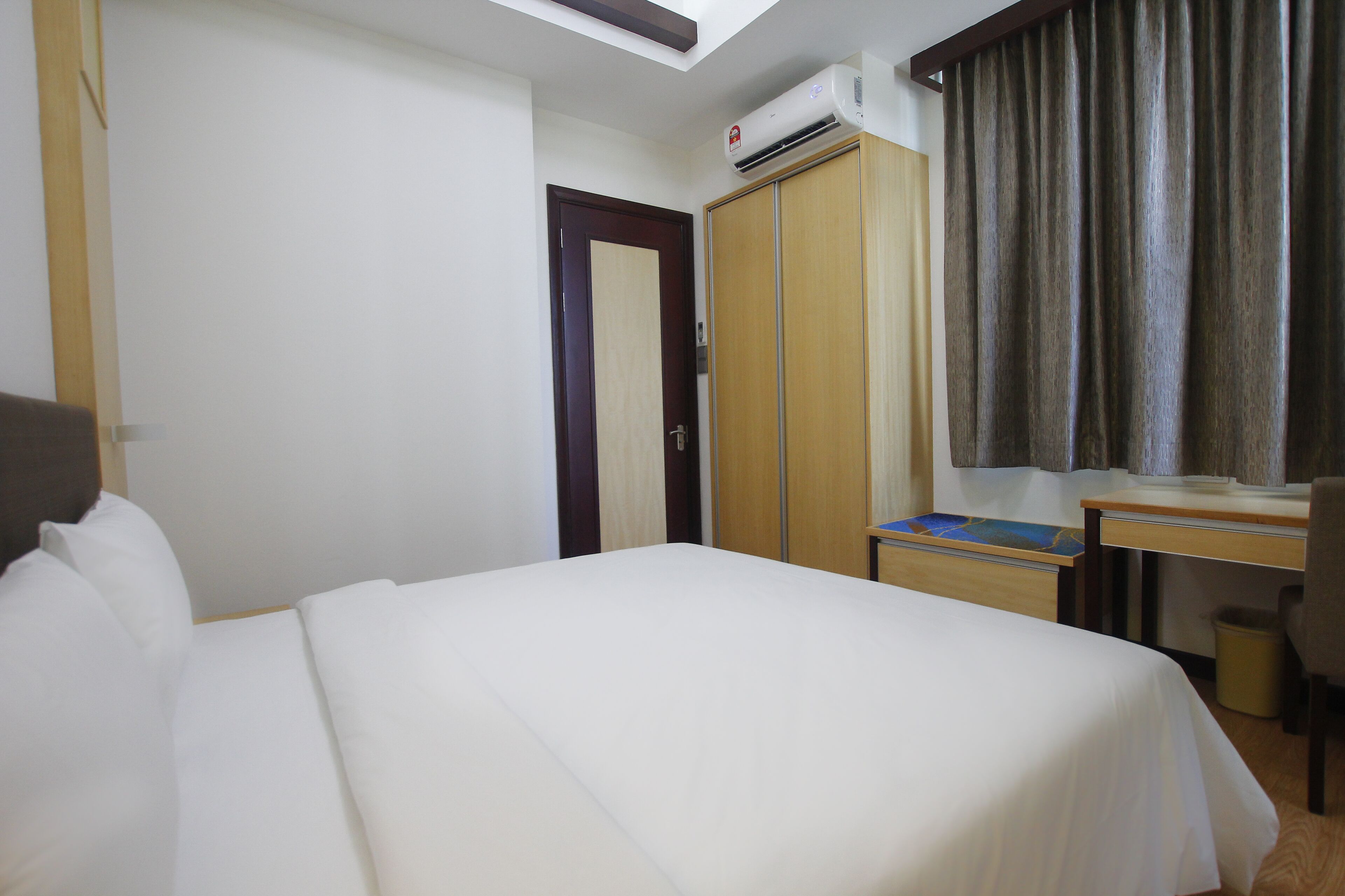 Una habitación de hotel con cama, escritorio, armario y aire acondicionado.