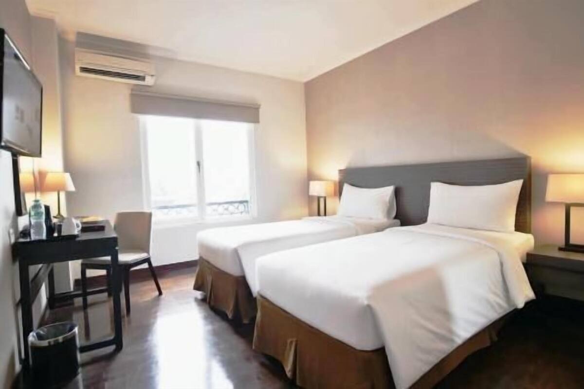 Een hotelkamer met twee bedden, een bureau, een stoel en een raam.