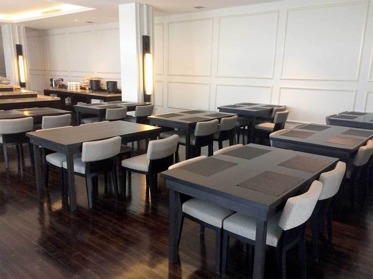 A modern dining area with multiple tables and chairs, a bar area, and a kitchen in the background.