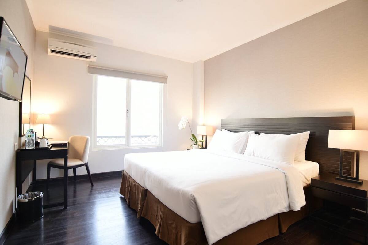 Une chambre d’hôtel avec un lit, un bureau, une chaise, une lampe et une fenêtre.
