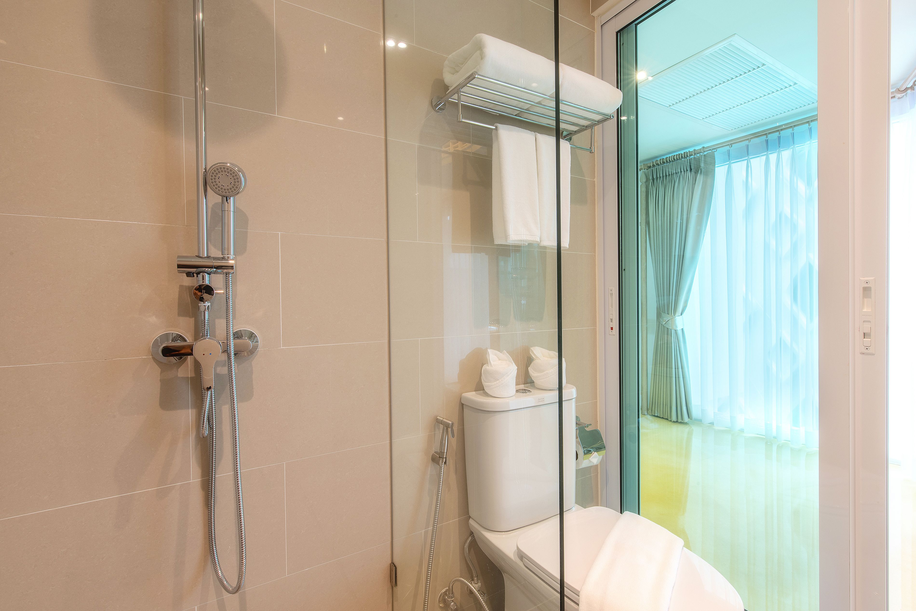 A modern bathroom with a glass shower enclosure, a toilet, and a glass door leading to a balcony with a curtain.