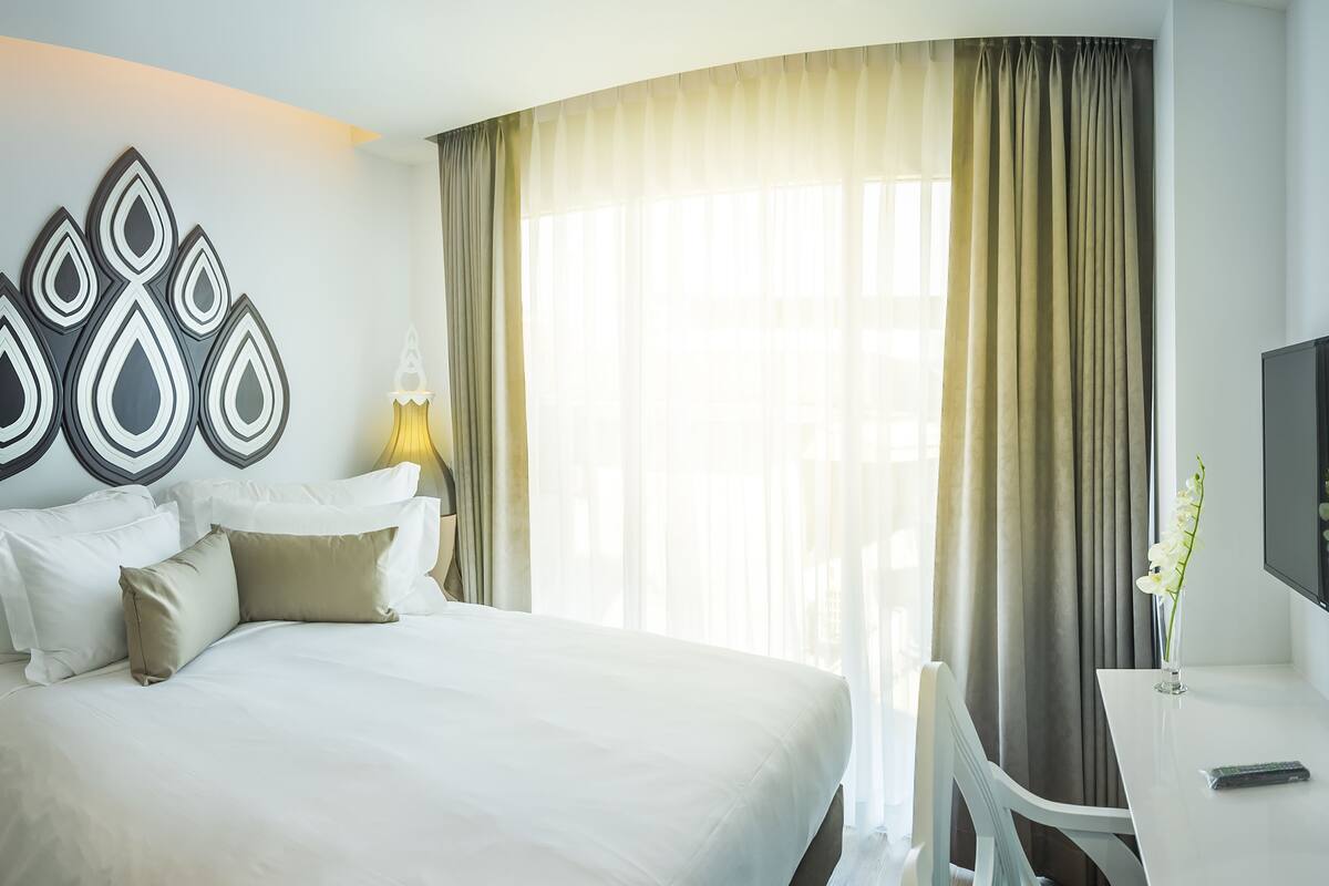 A hotel room with a large bed, a desk, a TV, and a decorative wall piece.