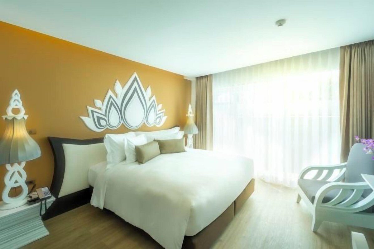 A hotel room with a bed, bedside lamps, a chair, and a window with curtains.