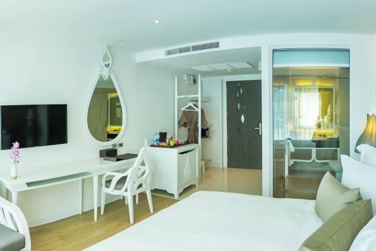 Ett hotellrum med en säng, ett skrivbord med en stol, en tv, en spegel och en garderob.