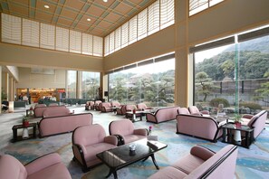 A spacious lobby with multiple seating areas, large windows offering a view of a mountainous landscape, and a reception desk in the background. - Kotosankaku Hotel (Kotohira)