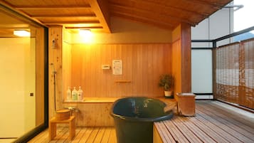 Una sauna de madera con un banco, un balde grande y una planta en maceta.
