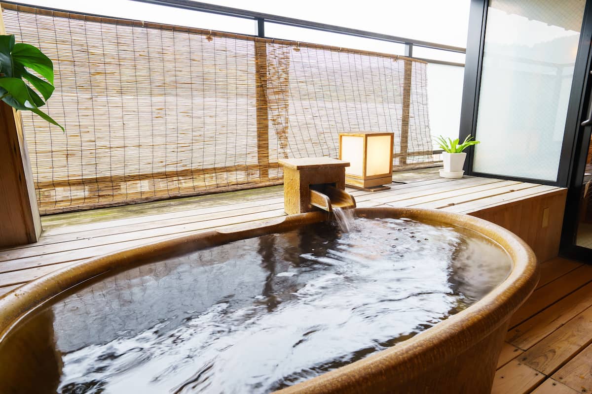 Ein Whirlpool mit Holzterrasse, einer kleinen Holzhütte und einem Blumentopf.