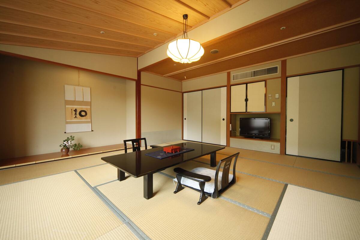 Ein traditioneller japanischer Raum mit Tatami-Boden, einem niedrigen Tisch, einer Couch und einem Fernseher.