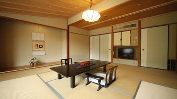 A traditional Japanese room with tatami flooring, a low table, a sofa, and a television.