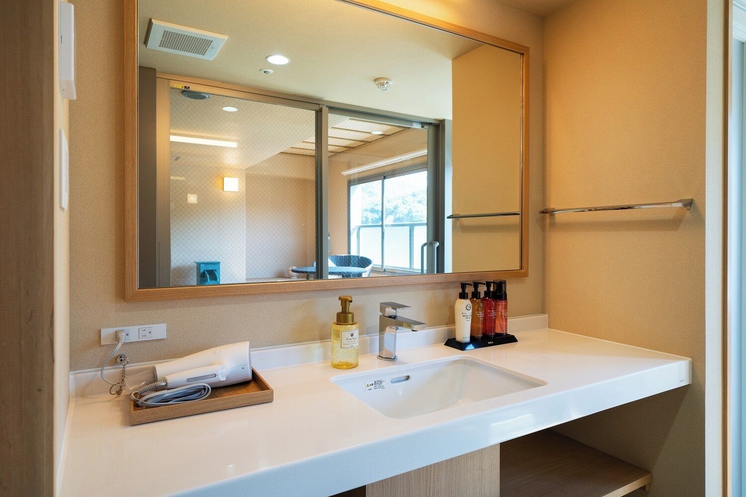 A modern bathroom with a large mirror, a white sink, and a towel rack.