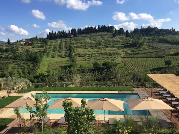 A pool area with multiple umbrellas and lounge chairs, surrounded by terraced fields and a hillside. - Borgo Del Cabreo (Greve in Chianti)