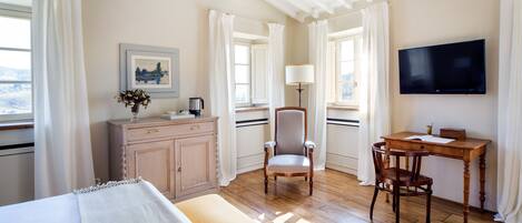 A hotel room with a bed, a desk, a chair, a TV, and a window with curtains.