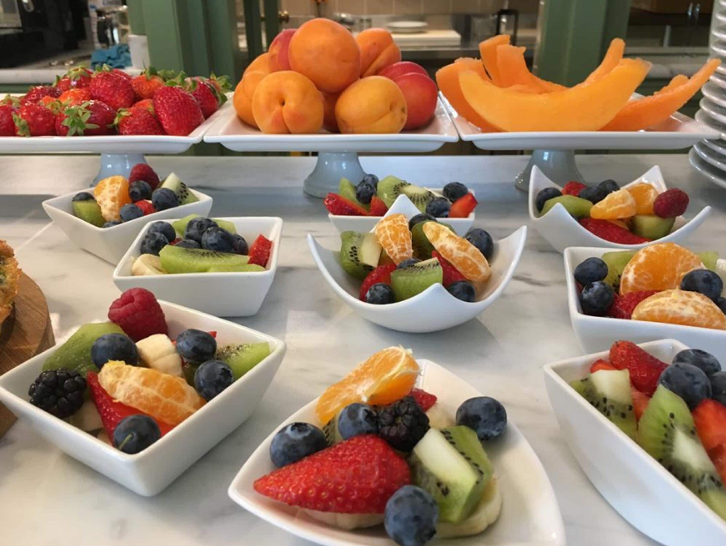 A buffet table with various fruit bowls and a plate of peaches.