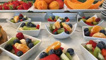 A buffet table with various fruit bowls and a plate of peaches.