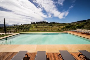 A rectangular pool with a wooden deck in the foreground and a vineyard landscape in the background. - Borgo Del Cabreo (Greve in Chianti)