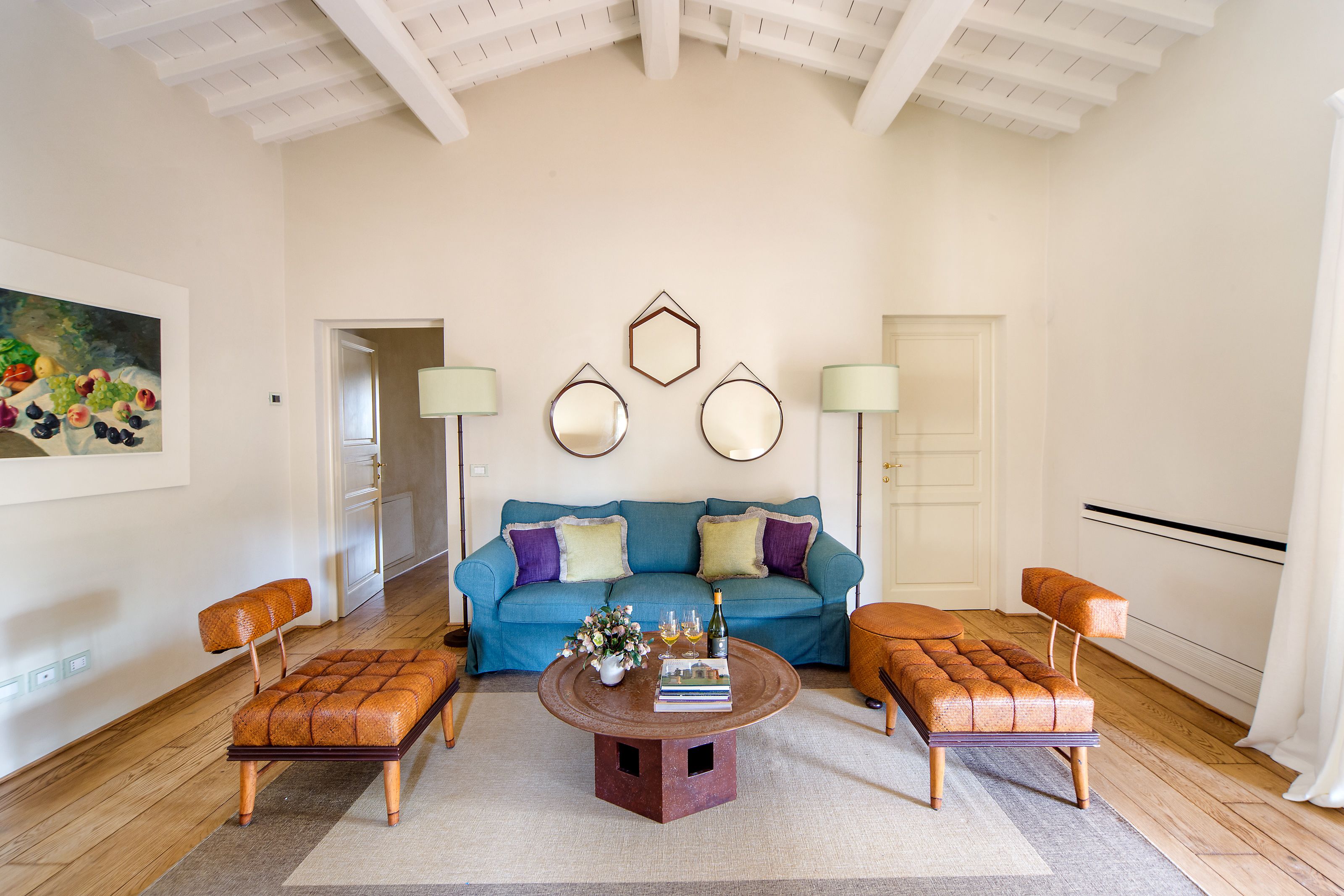 A spacious living room with a blue sofa, two ottomans, a coffee table, and a painting on the wall.