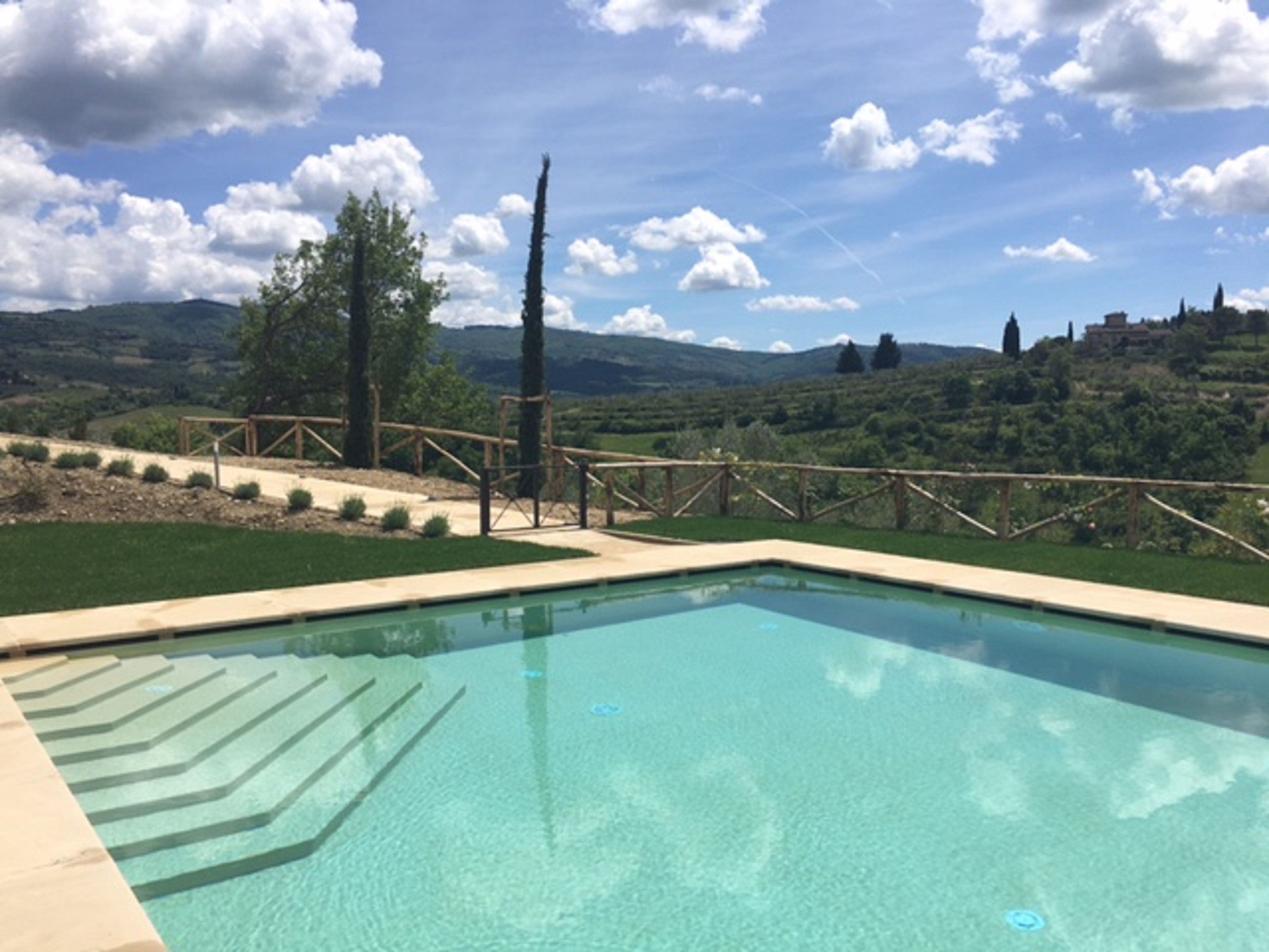 Ein klares Schwimmbecken mit Blick auf eine hügelige Landschaft und einen Holzzaun.