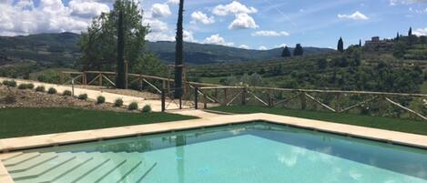 Ein klares Schwimmbecken mit Blick auf eine hügelige Landschaft und einen Holzzaun.