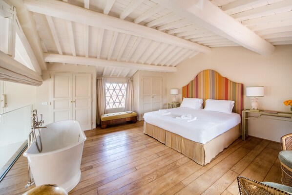 A spacious bedroom with a large bed, a bathtub, and a wooden ceiling.