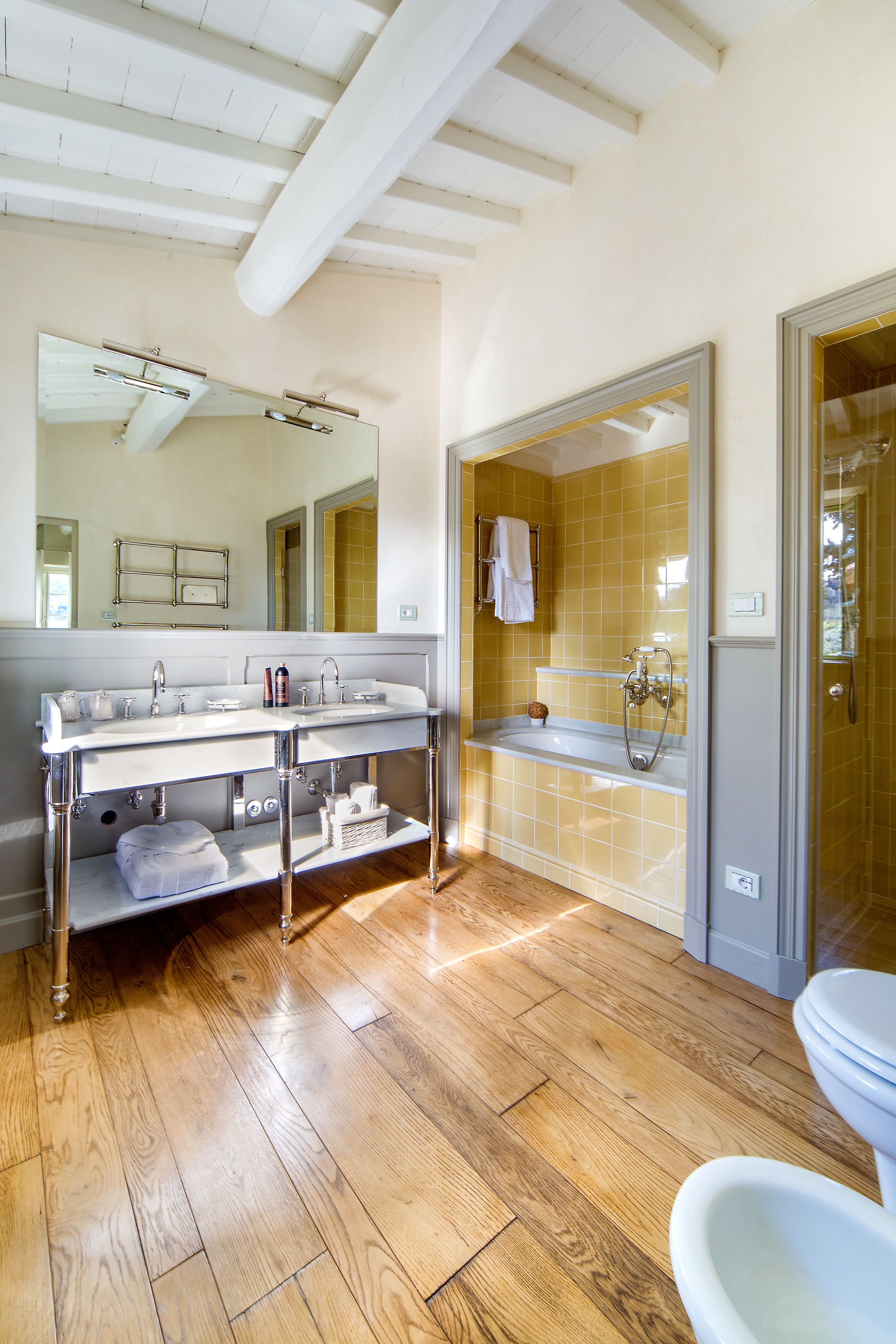 A bathroom with a wooden floor, a double sink vanity, a bathtub, and a toilet.