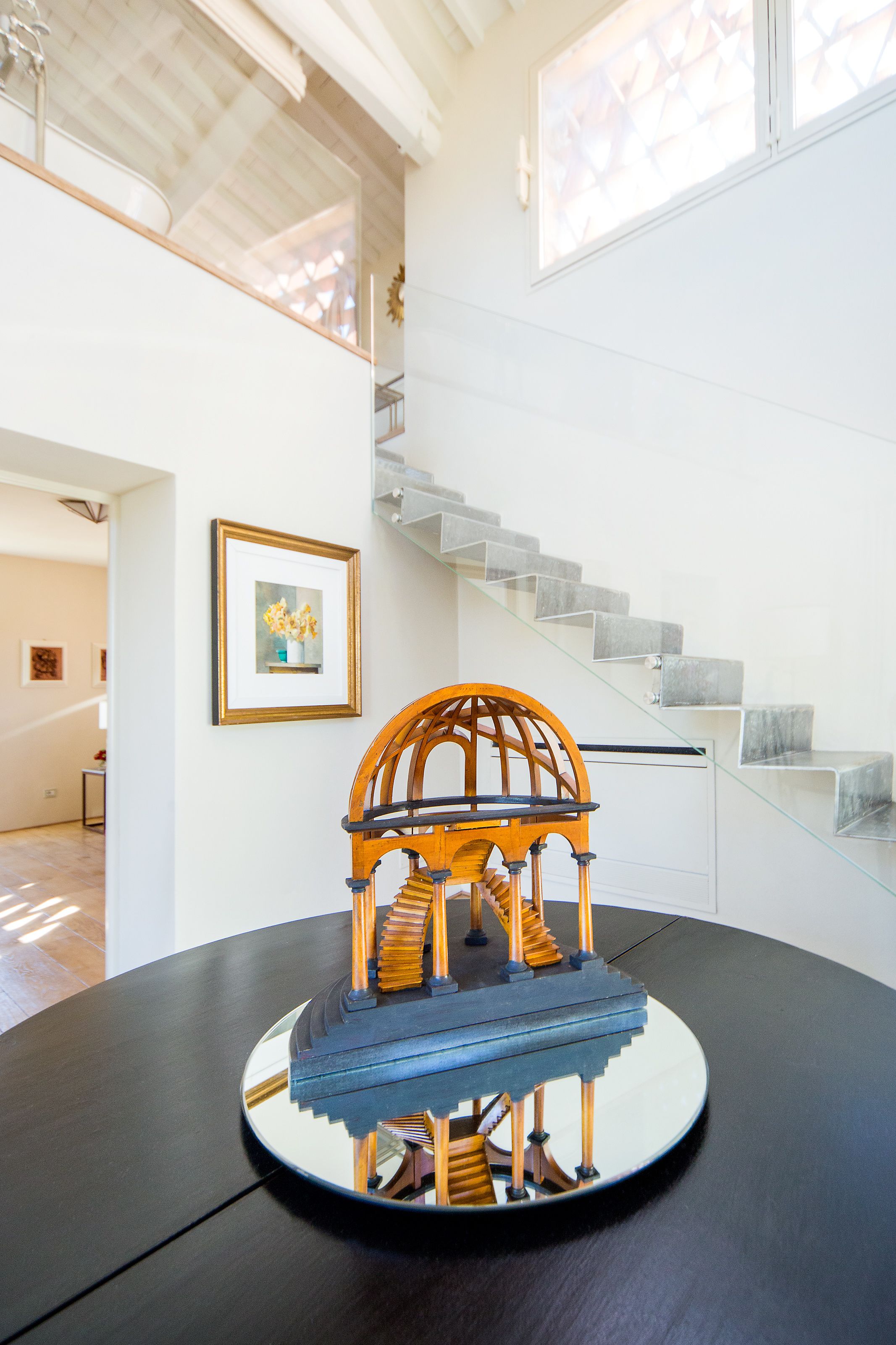A model of a wooden gazebo on a table, a staircase, and a framed picture on the wall.
