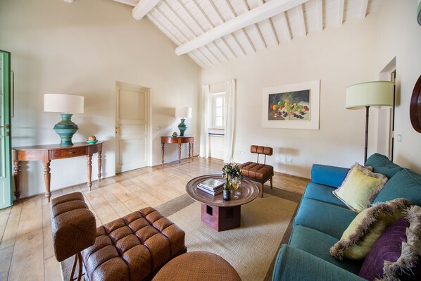 A spacious living room with a wooden floor, a blue sofa, a round coffee table, and a wooden desk with a lamp. - Borgo Del Cabreo (Greve in Chianti)
