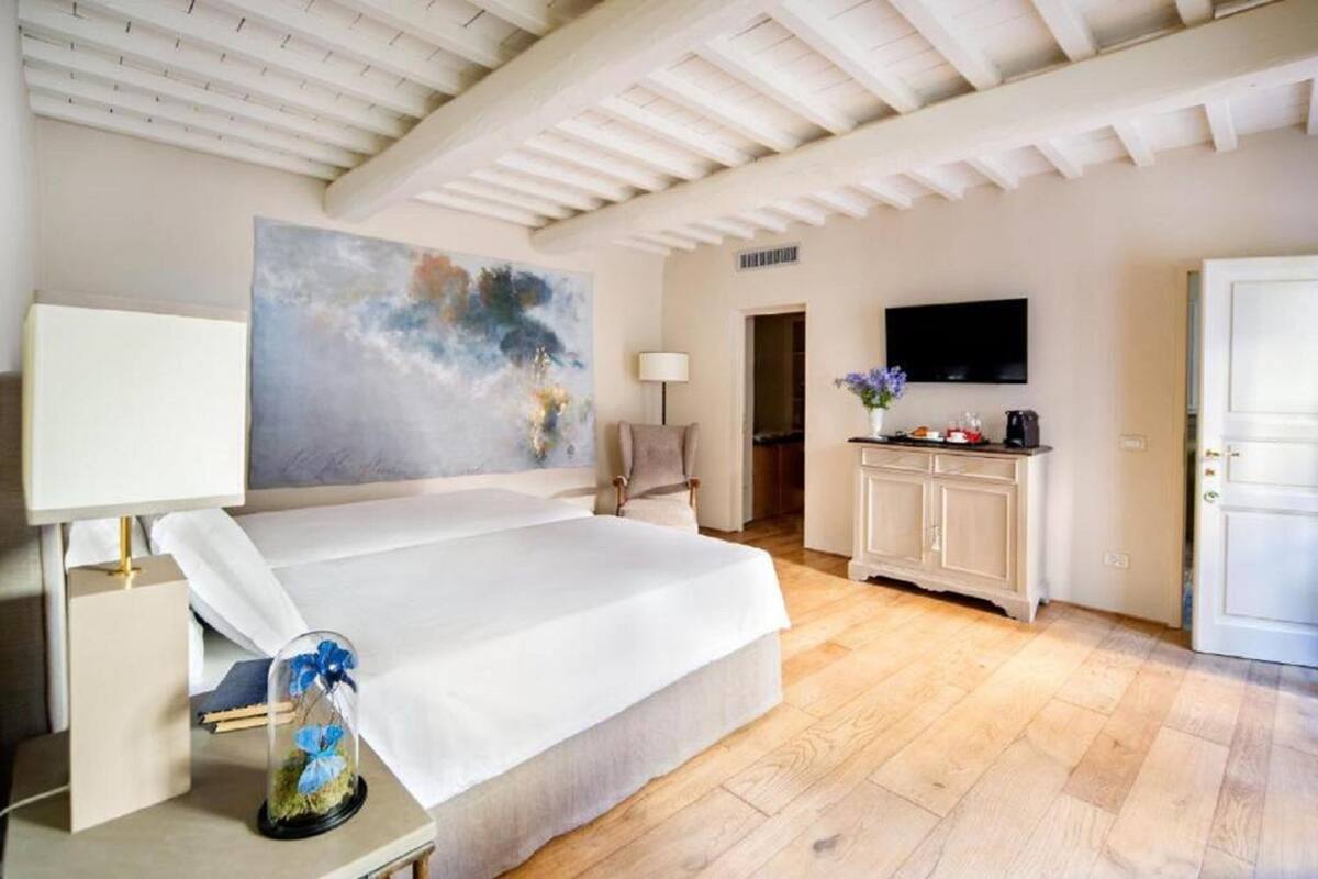 Un dormitorio con una cama grande, un cuadro en la pared, un televisor y un aparador con un jarrón de flores.
