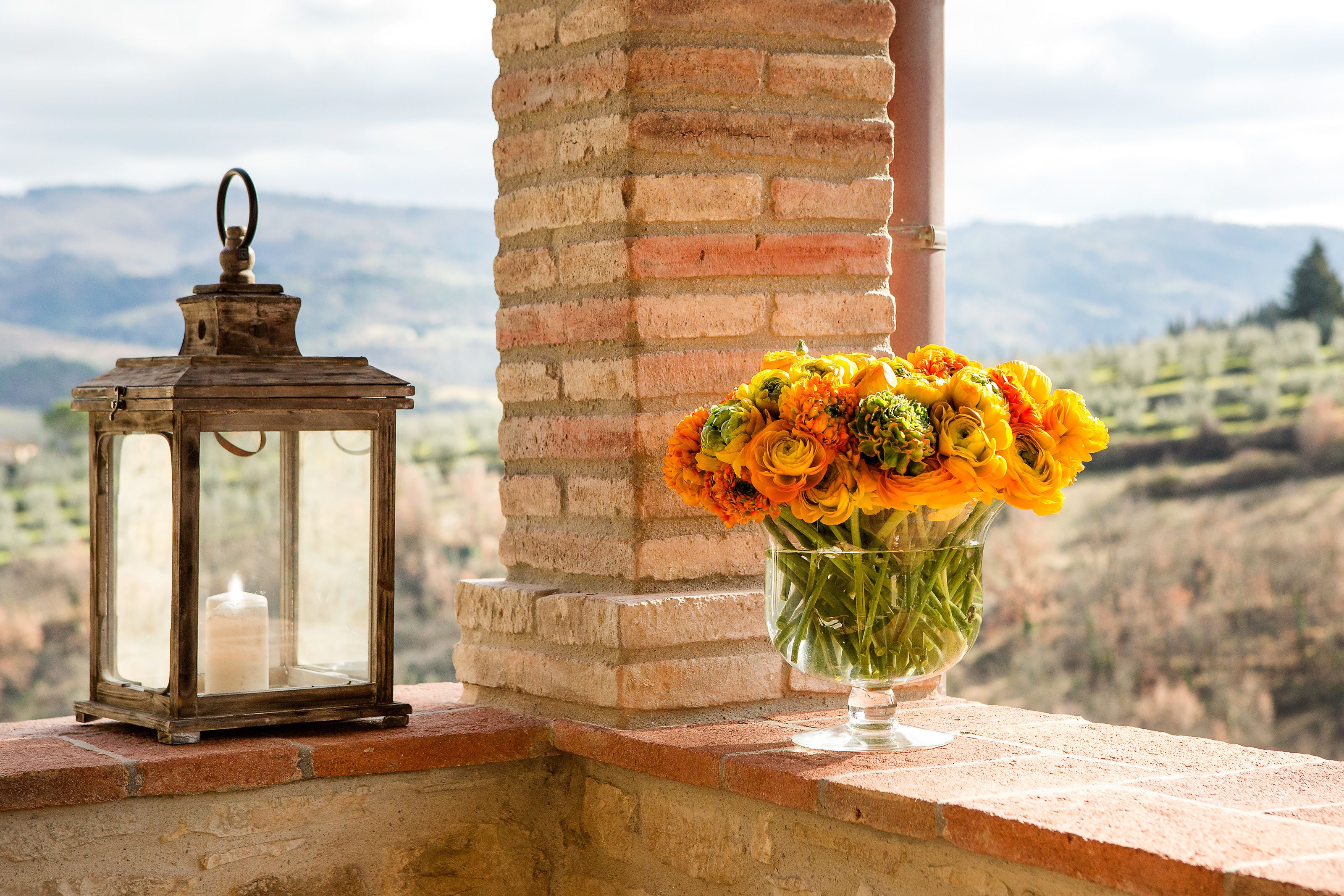 A lantern and a vase of flowers on a ledge with a mountain view.
