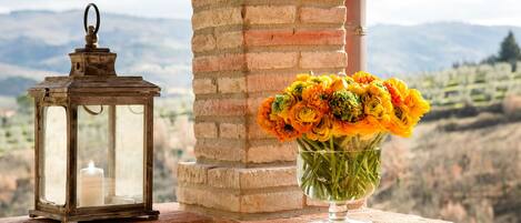 A lantern and a vase of flowers on a ledge with a mountain view.