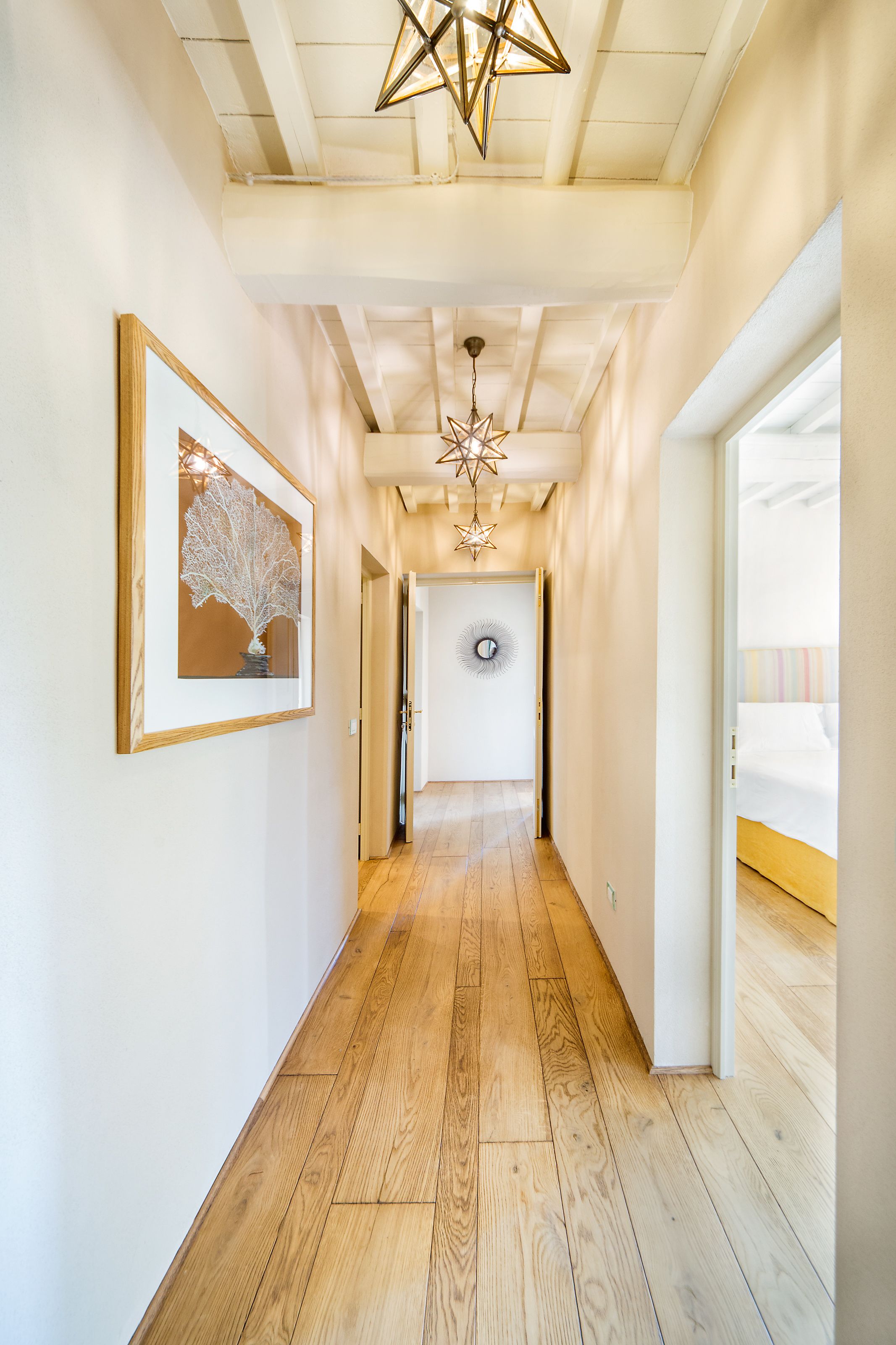 A hallway with wooden flooring, a framed artwork, a star-shaped light fixture, and a door with a circular mirror.
