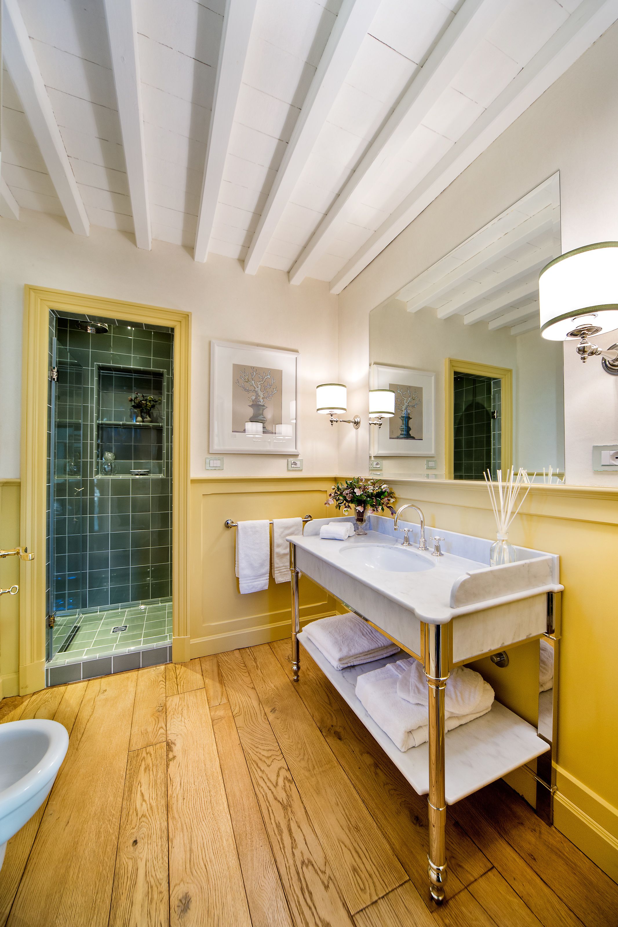 A bathroom with a wooden floor, a white sink with a mirror above it, and a shower with a glass door.
