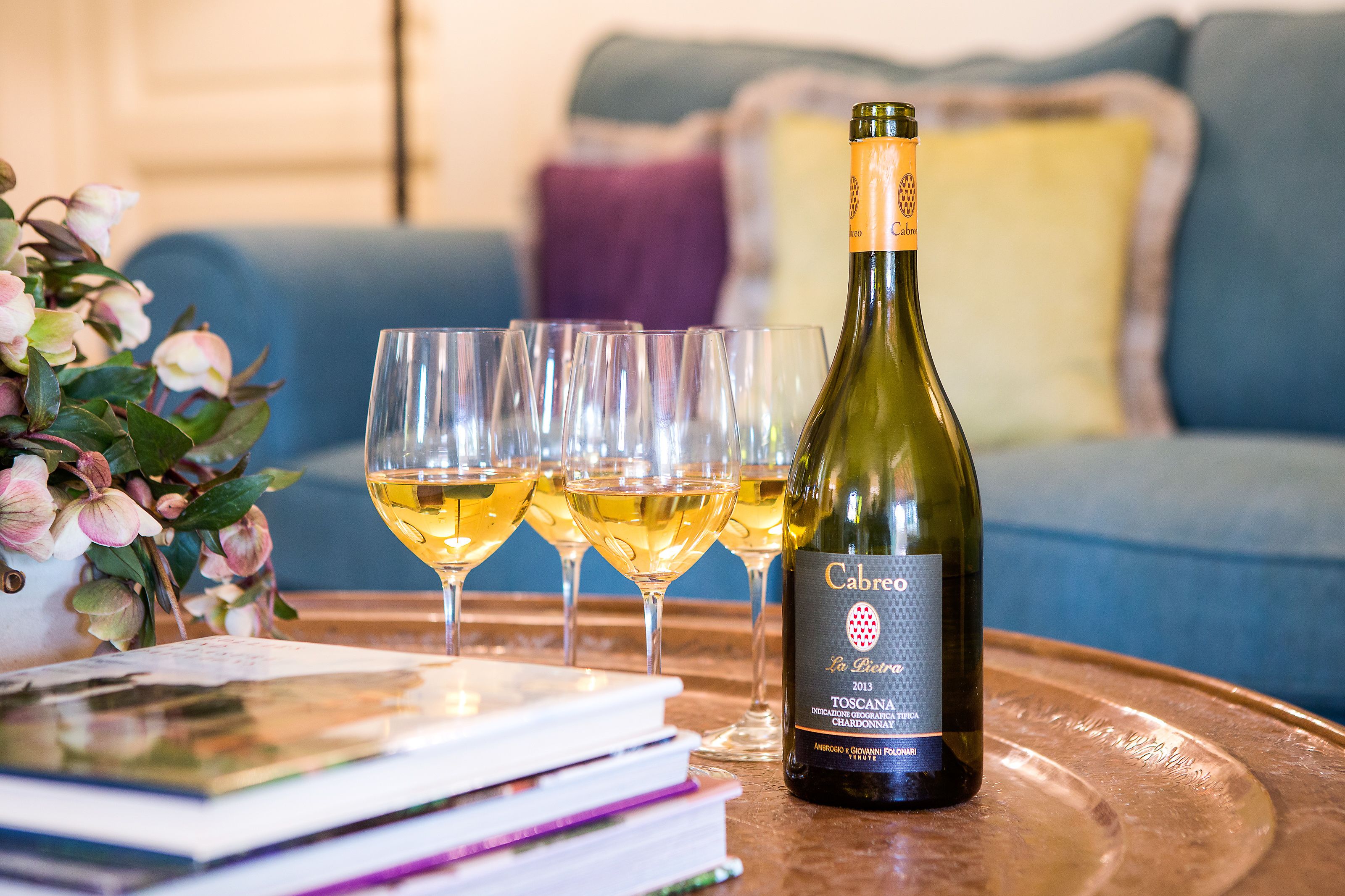 A bottle of wine and several glasses on a table, with a sofa and cushions in the background.